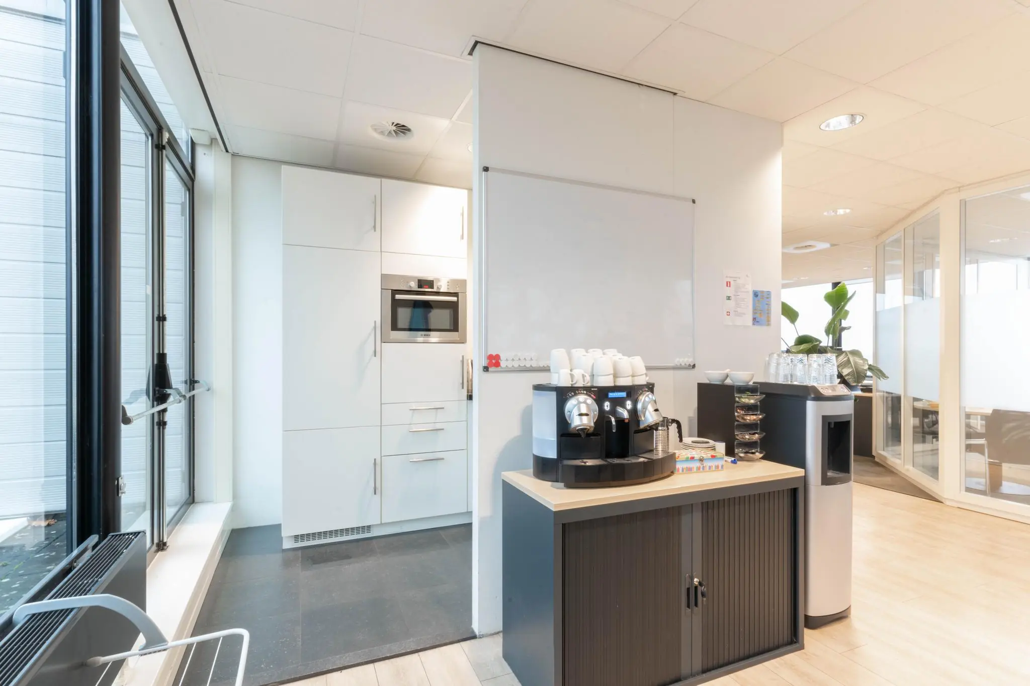 Moderne kantoorpantry met een koffieautomaat, servies en ingebouwde magnetron.